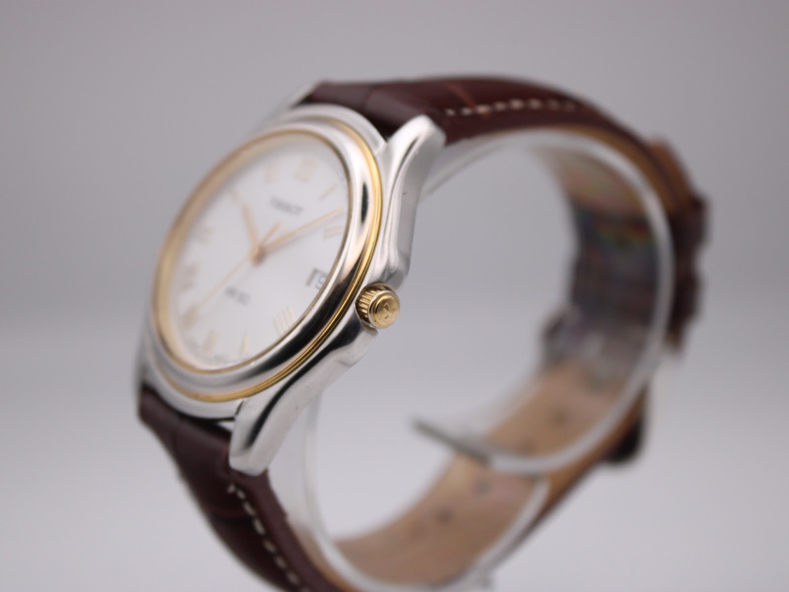 Side angle view of Tissot PR 50 watch showing the gold PVD bezel and crown, with brown leather strap.