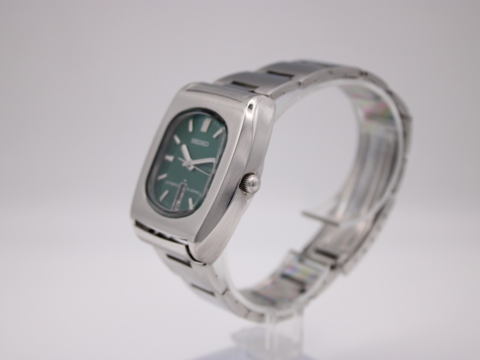 Side view of the Seiko 7006-5070 showing the profile of the stainless steel case and integrated bracelet on a clear stand.