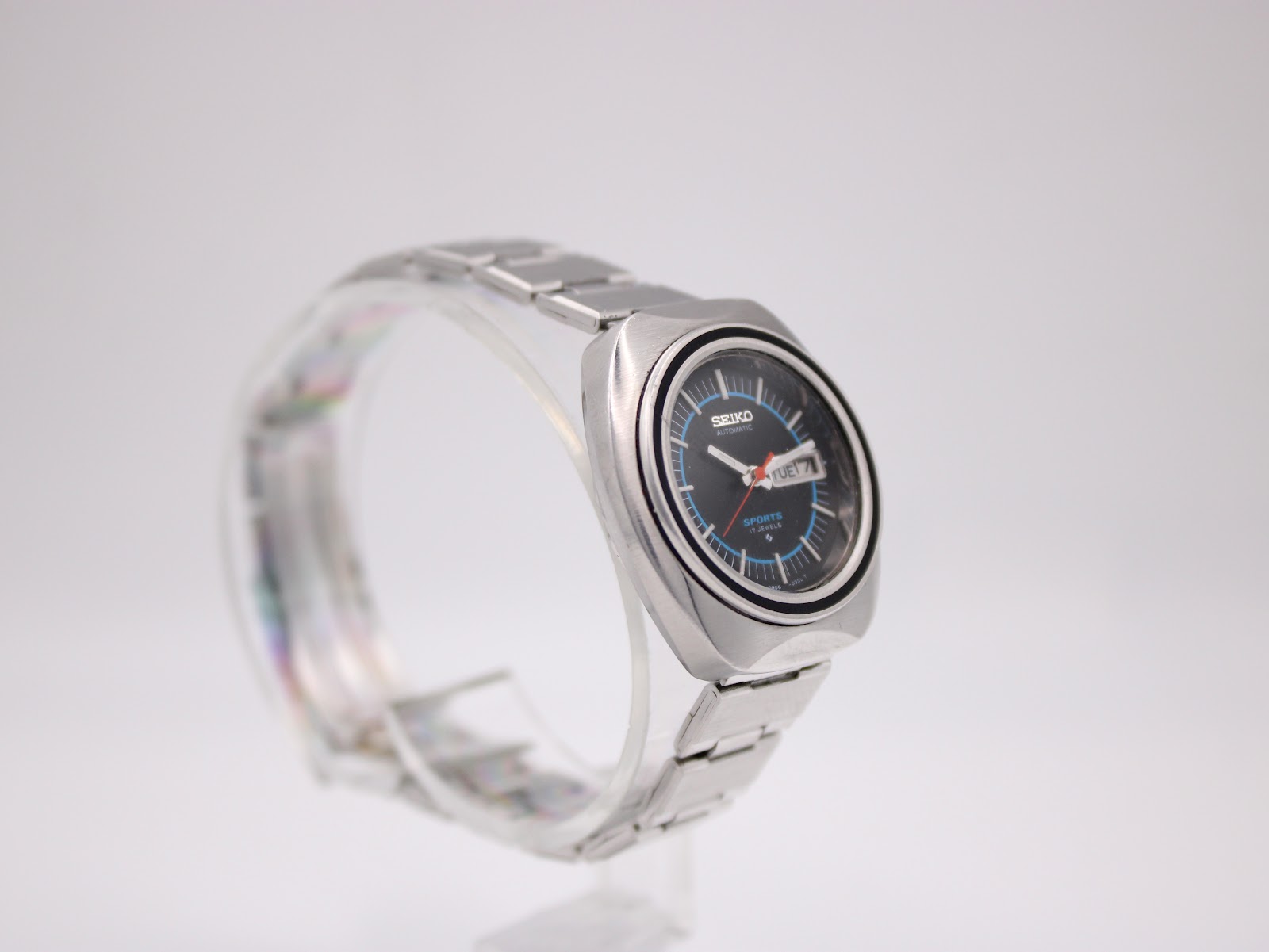 Close-up of matte black dial showing applied silver baton indices, red seconds hand, dual-language day-date aperture, and Seiko automatic branding