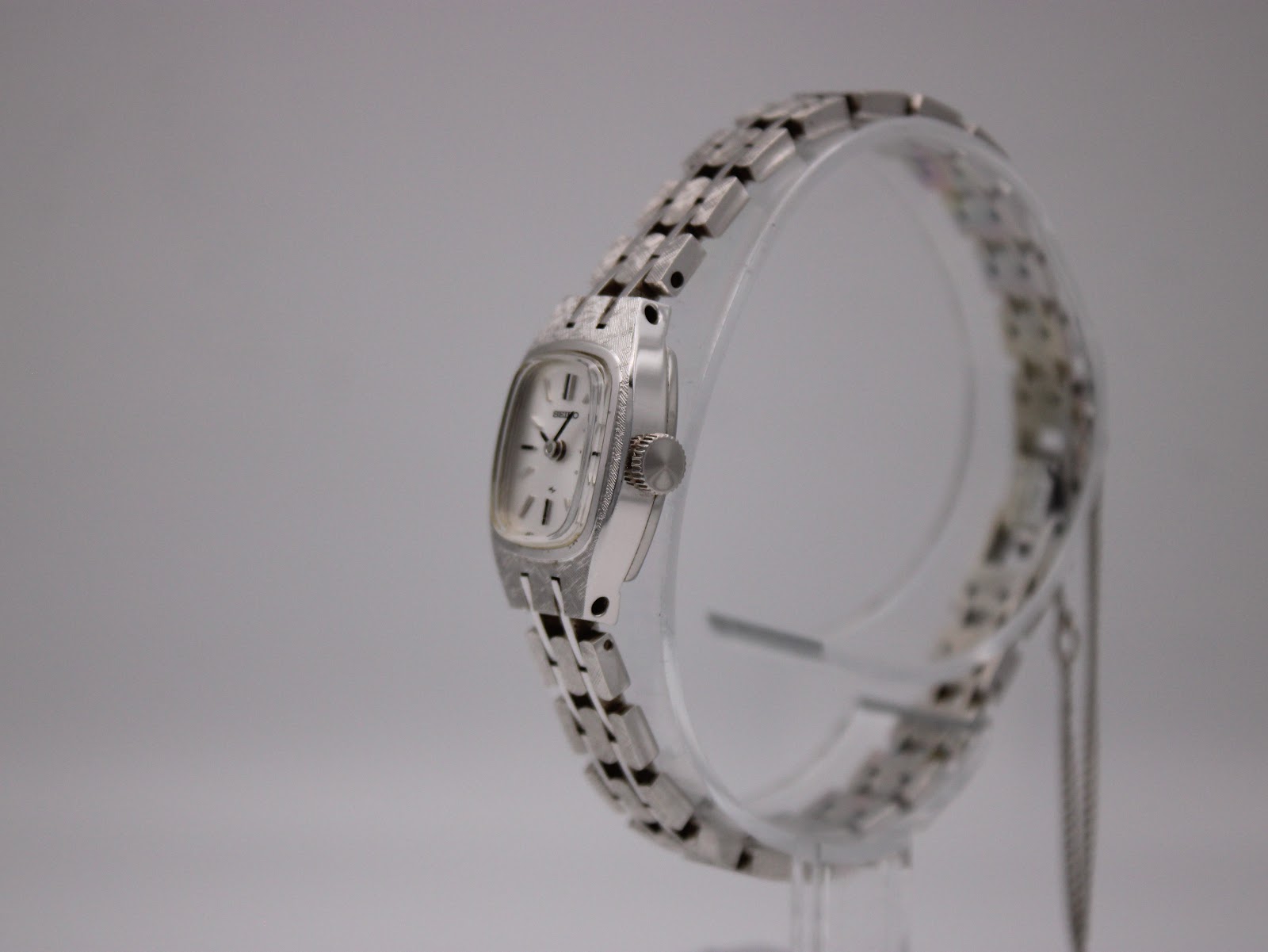 Side view of the Seiko 2N0372 watch on a clear stand, highlighting the crown and the textured finish of the case and bracelet links.