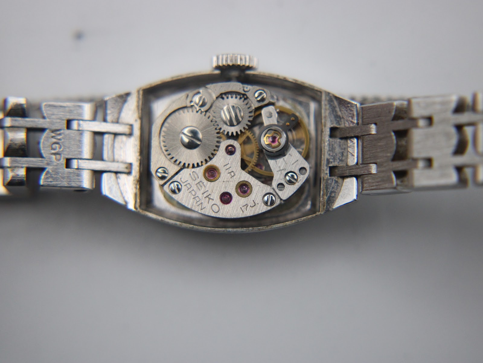 Close-up of the open watch case back revealing the mechanical hand-wind movement, showing gears, jewels, and "SEIKO JAPAN 17J" engraving.