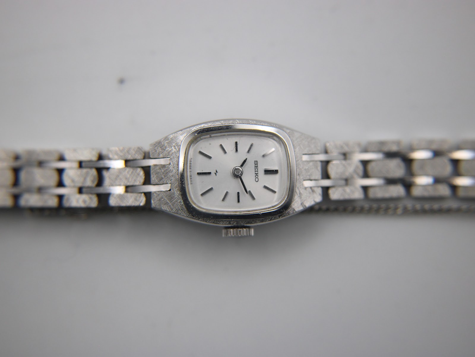 Top-down view of the Seiko watch dial and integrated bracelet, showing the silver face with black baton indices and hands.