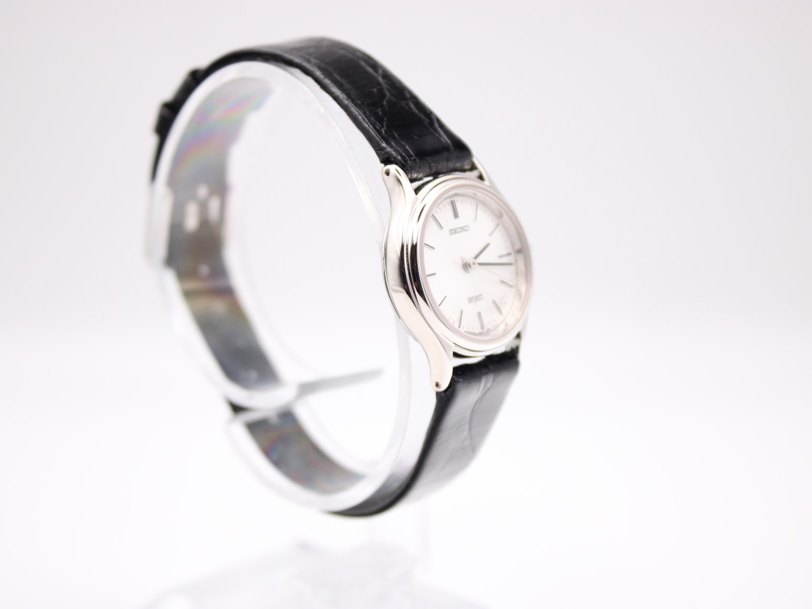 Angled side view of the Seiko Spirit watch, highlighting the case profile and black leather strap on a transparent stand.