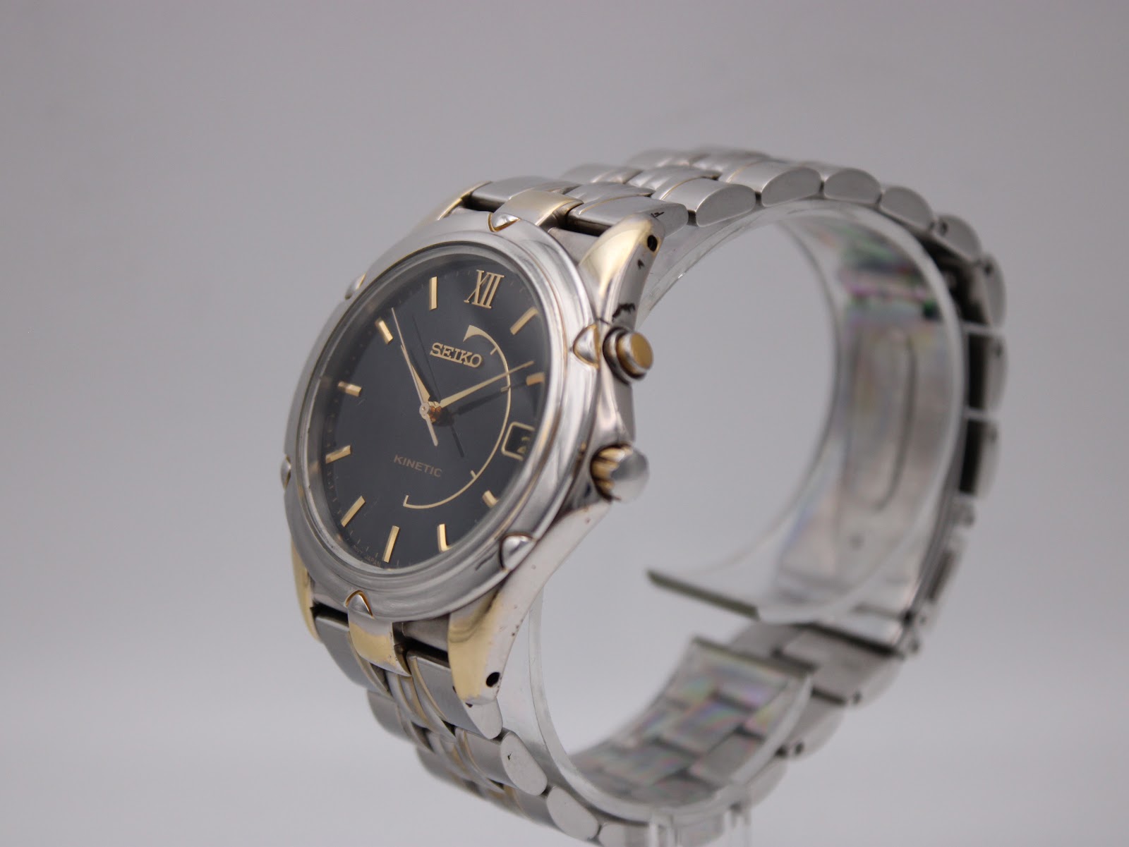 Angled left view of the Seiko Kinetic watch on a display stand, highlighting the two-tone case and bracelet design.