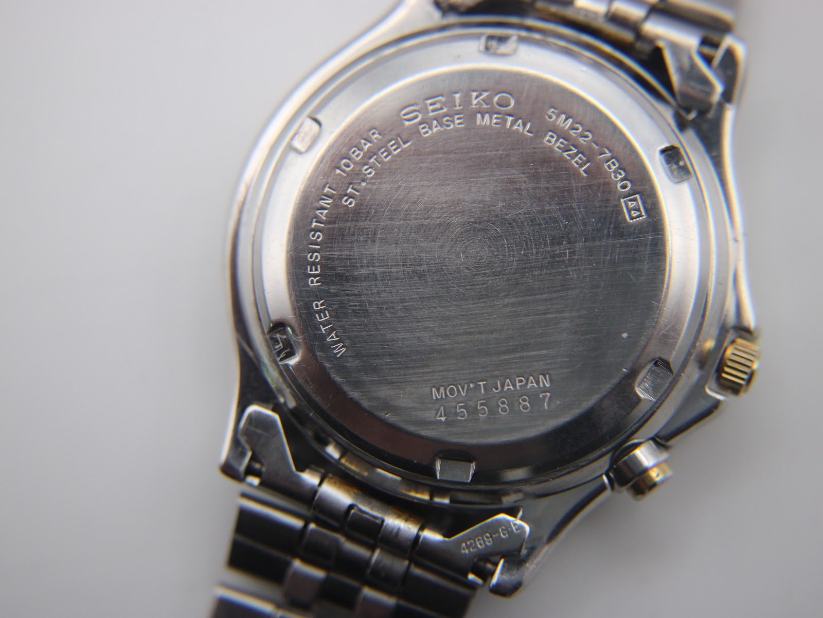 Close-up of the watch case back engraved with "SEIKO", "5M22-7B30", "WATER RESISTANT 10 BAR", and serial number "455887".