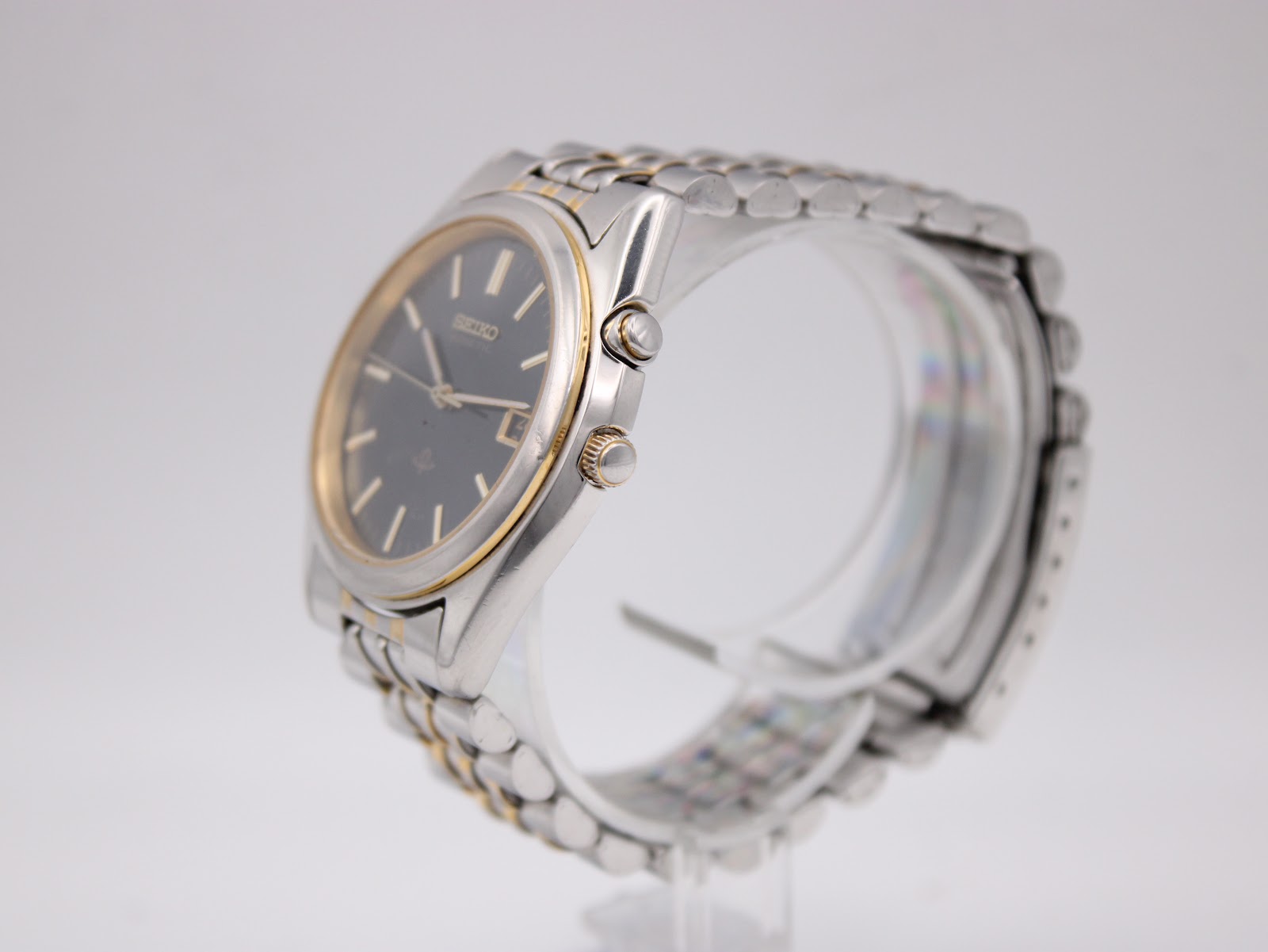 Angled side view of the Seiko watch, showing the silver case, gold-tone bezel, crown, and power reserve pusher.
