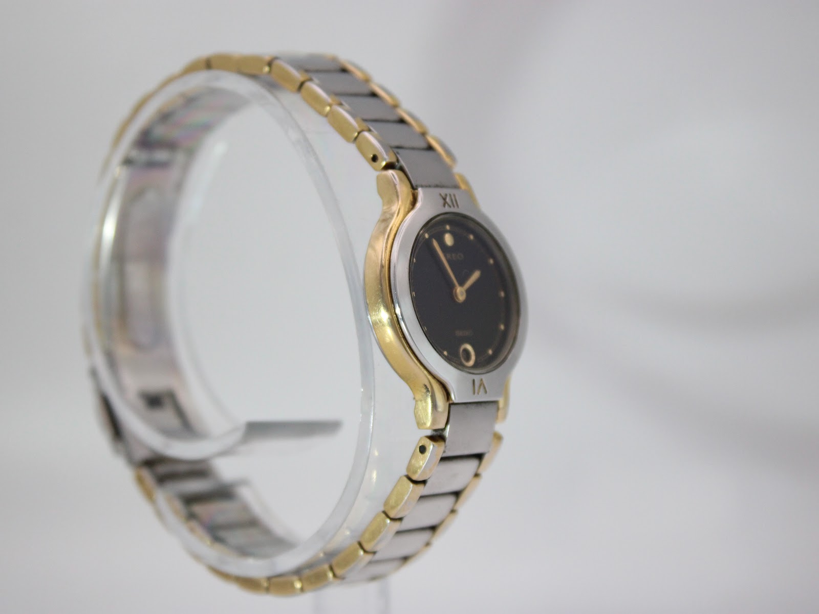 Opposite angled side view of the Seiko Creo watch, highlighting the two-tone bracelet design on a clear display stand.