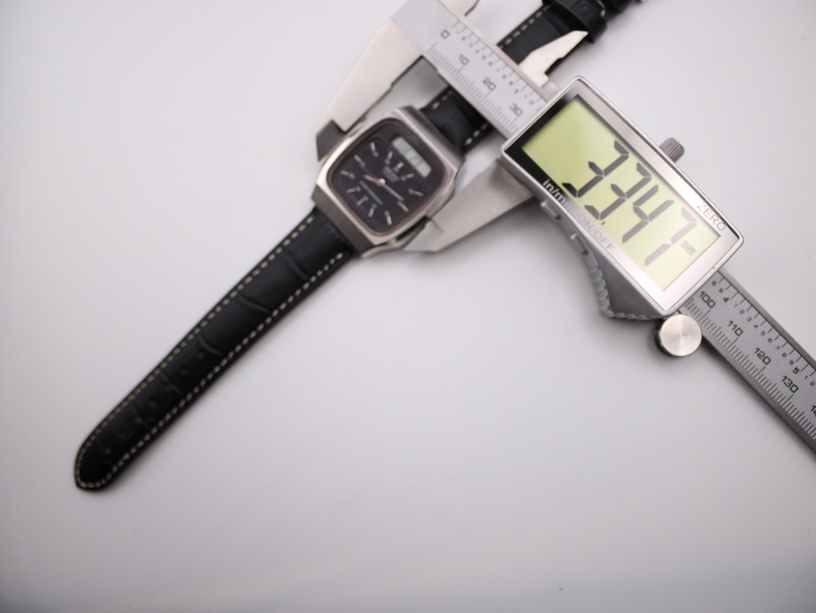 Overhead view of the Seiko H556-5030 watch case being measured by a digital caliper, displaying 33.47mm.