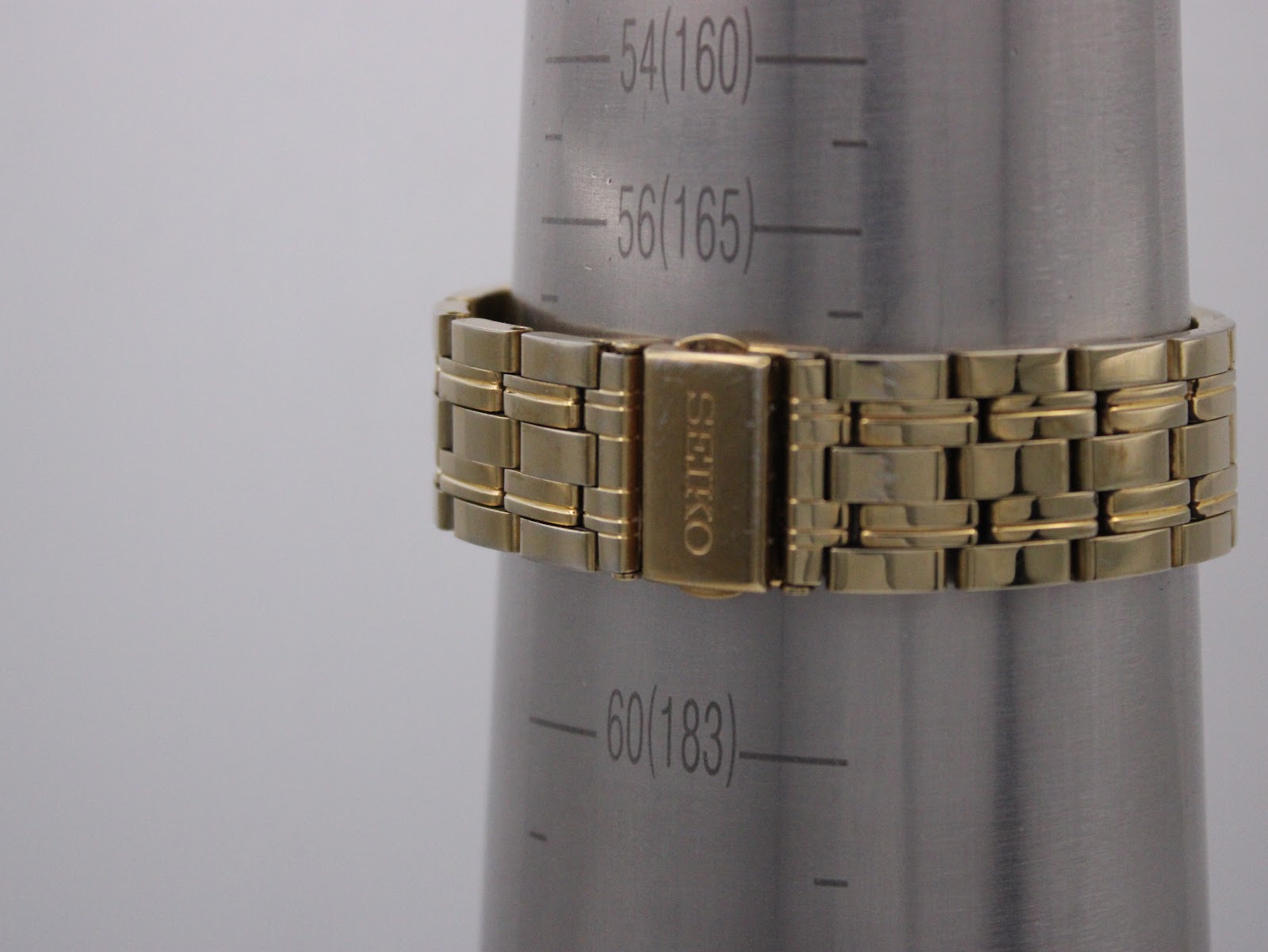 Close-up of the gold-tone steel bracelet clasp with "SEIKO" engraving, on a wrist sizing gauge indicating a circumference of approximately 16.5cm.