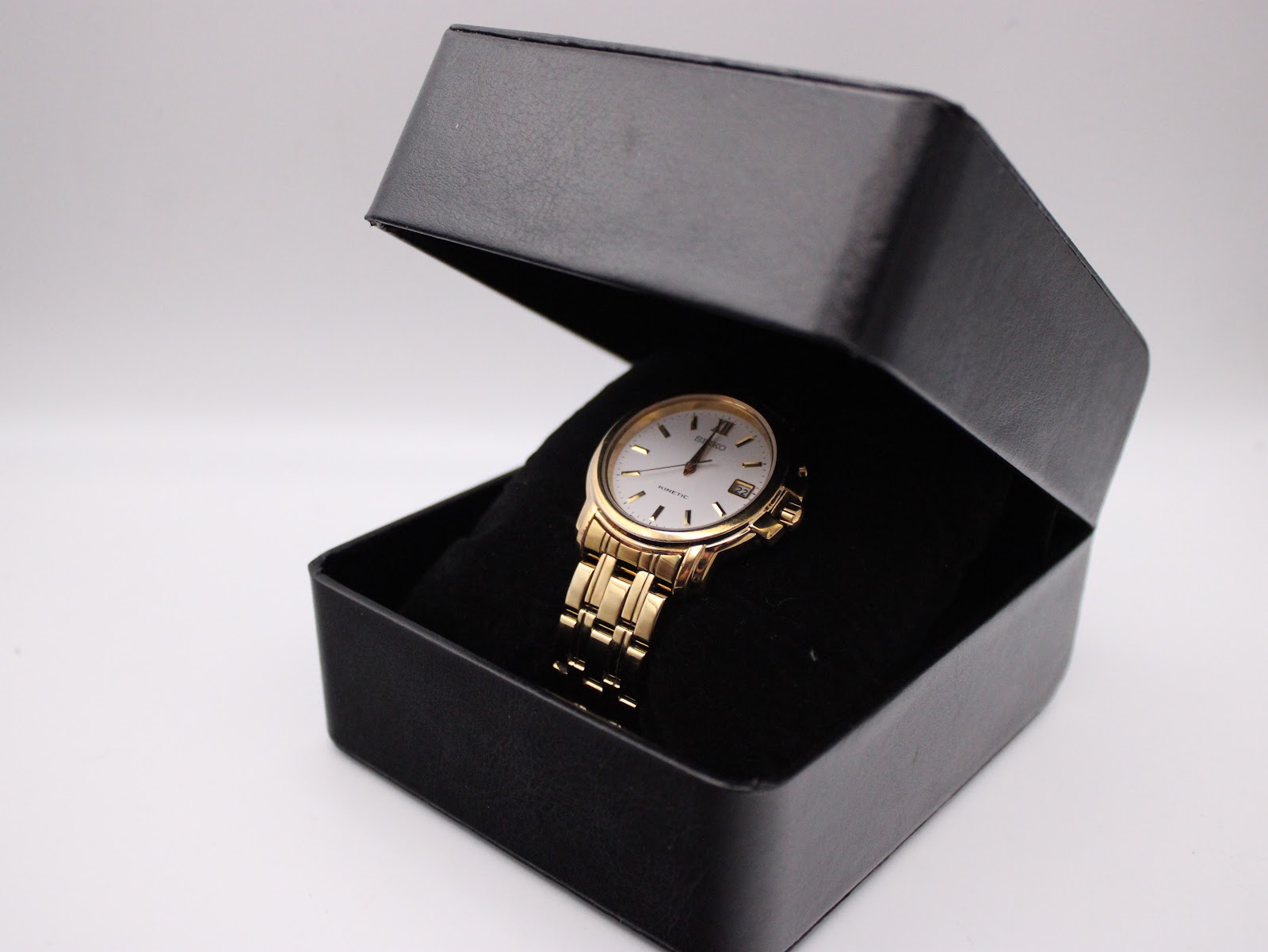 The gold-tone Seiko watch presented in an open black watch box, sitting on a soft black cushion.