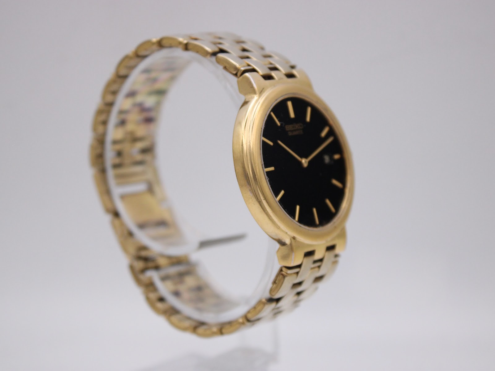 Angled side profile of the gold-tone Seiko 7N29-7A00 watch on a display stand.