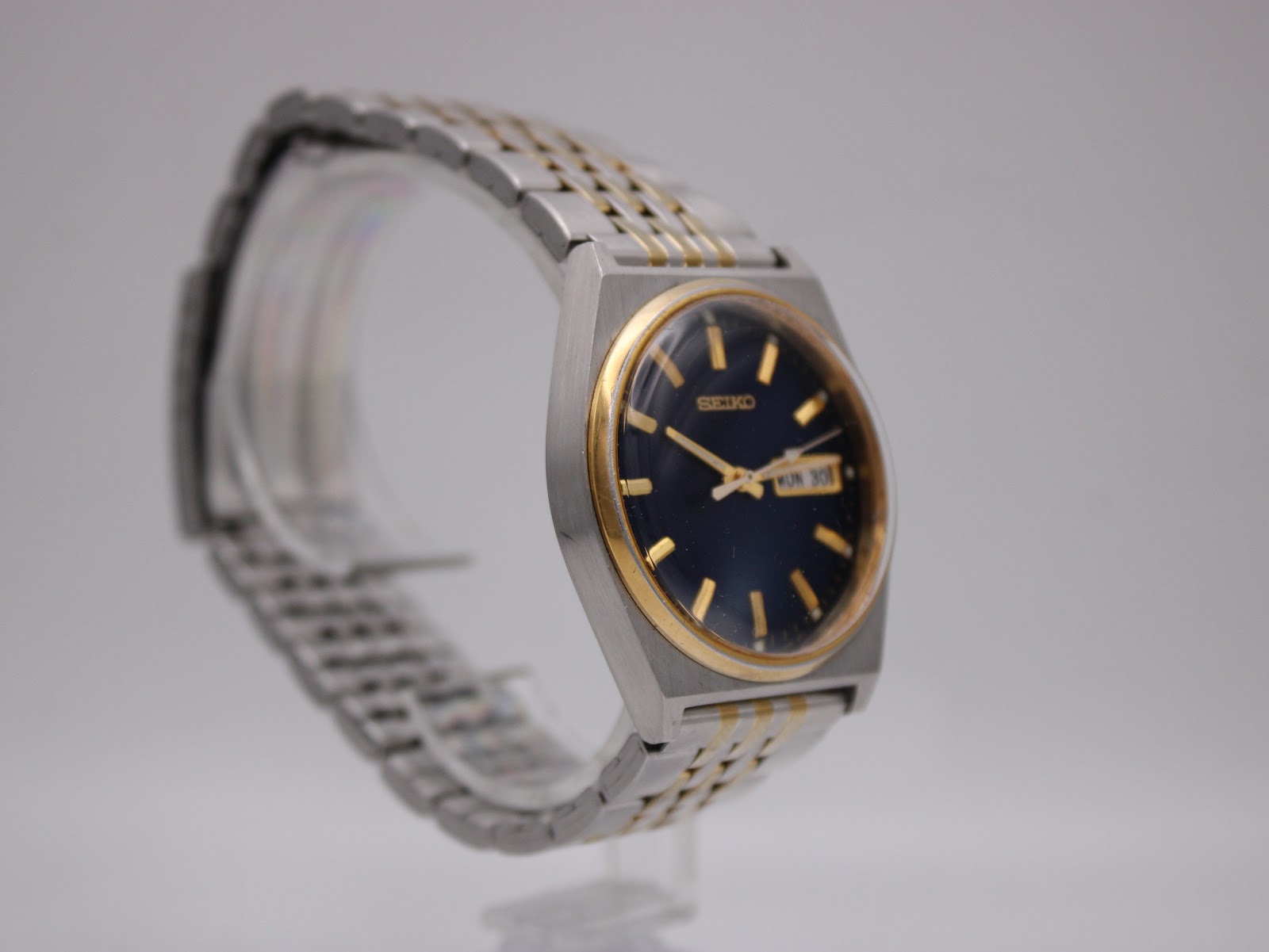 Angled view of the Seiko V743-9020 watch on a display stand, highlighting the two-tone integrated bracelet and case profile.