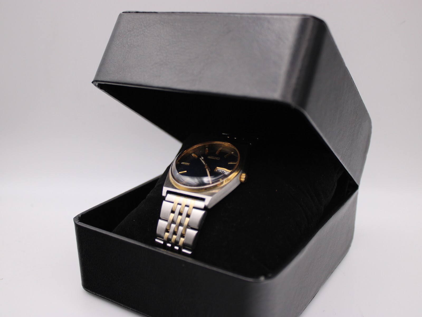 The Seiko V743-9020 two-tone watch nestled in a black velvet interior inside a black presentation box.