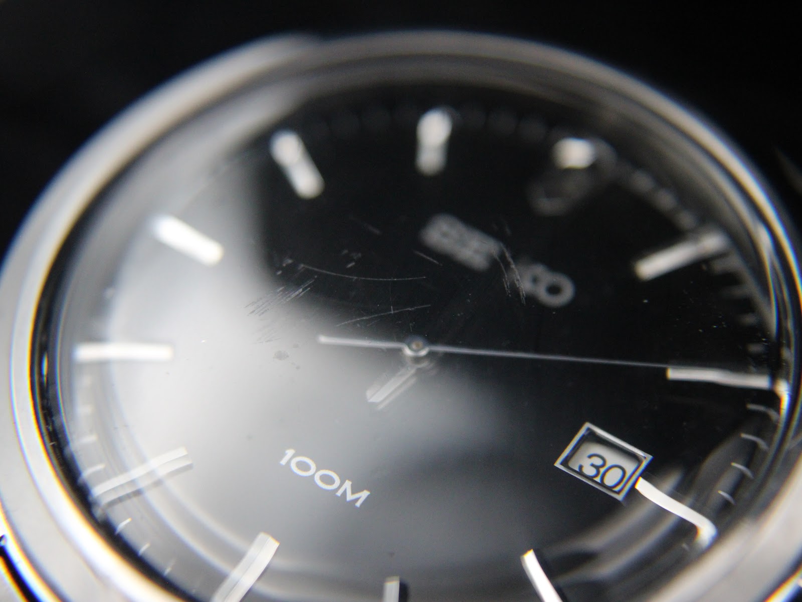 Close-up of the watch's black sunburst dial showing applied indices and visible crystal scratches.