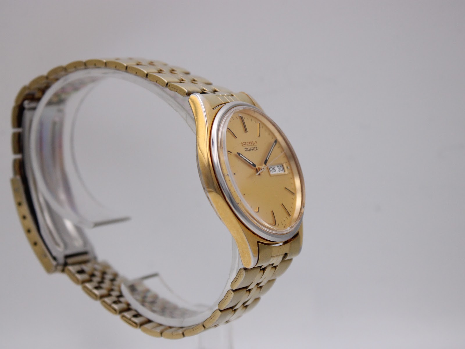 Another side profile of the Seiko watch on a clear stand, angled to show the full gold-tone integrated bracelet.