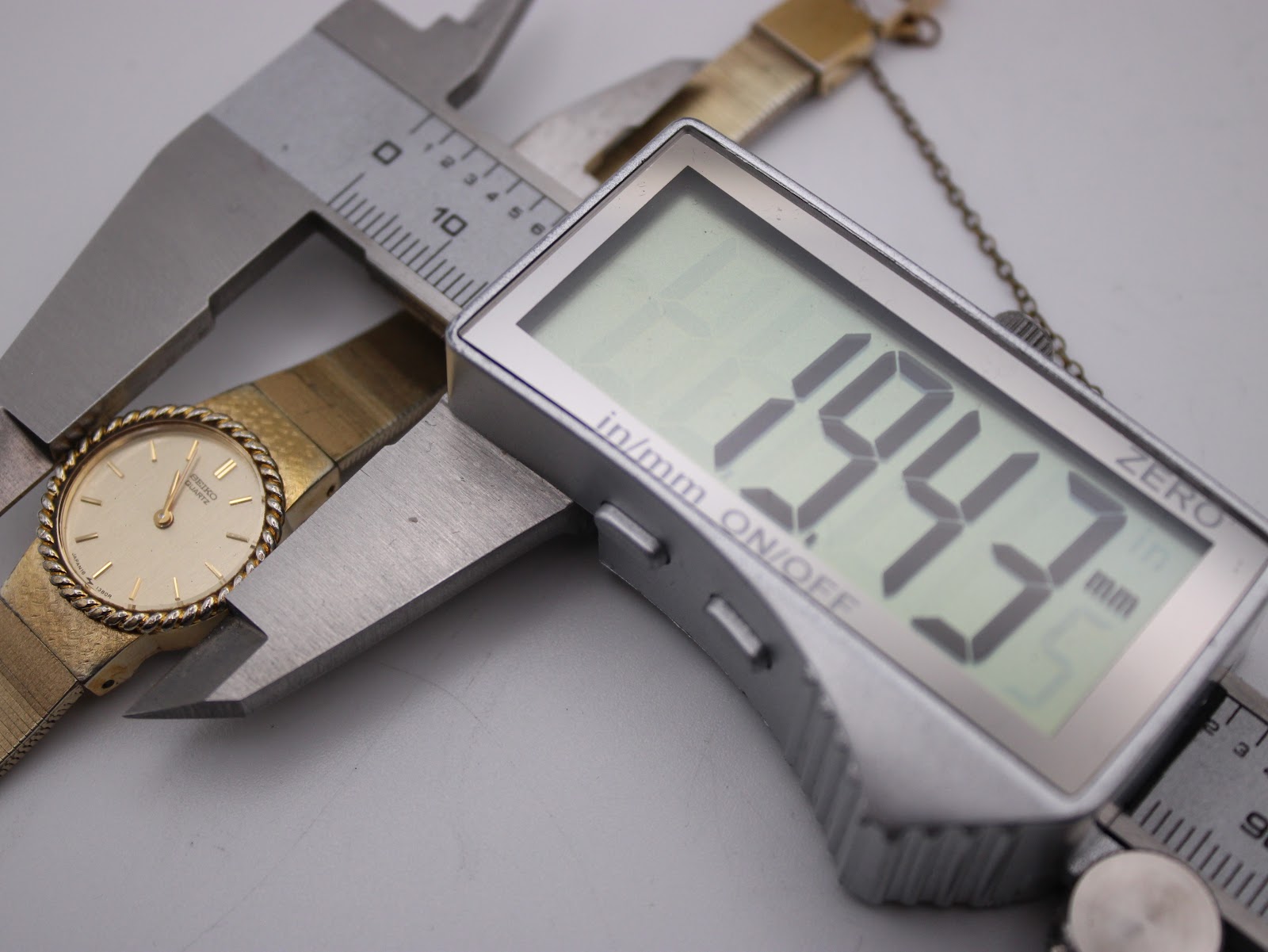 The Seiko watch being measured by a digital caliper, displaying a precise case diameter of 19.43mm.