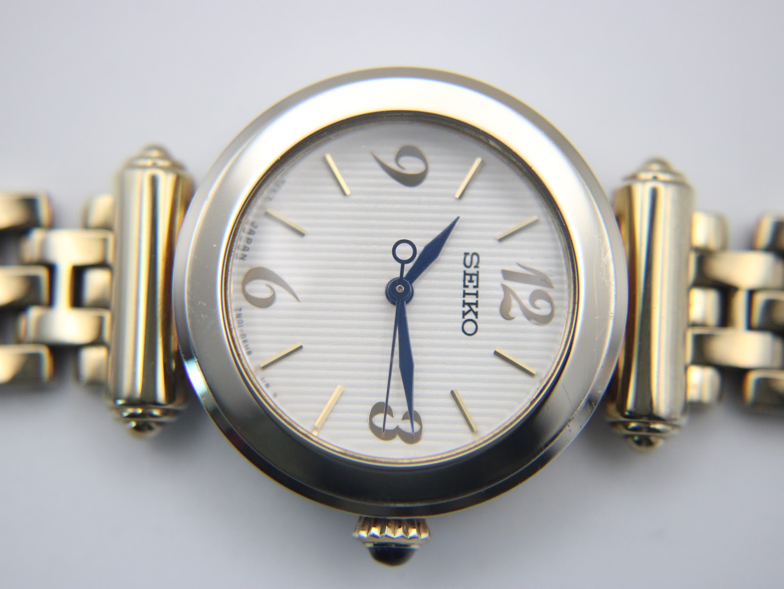 Macro shot of the Seiko white textured dial, showcasing applied gold markers and blue hands.