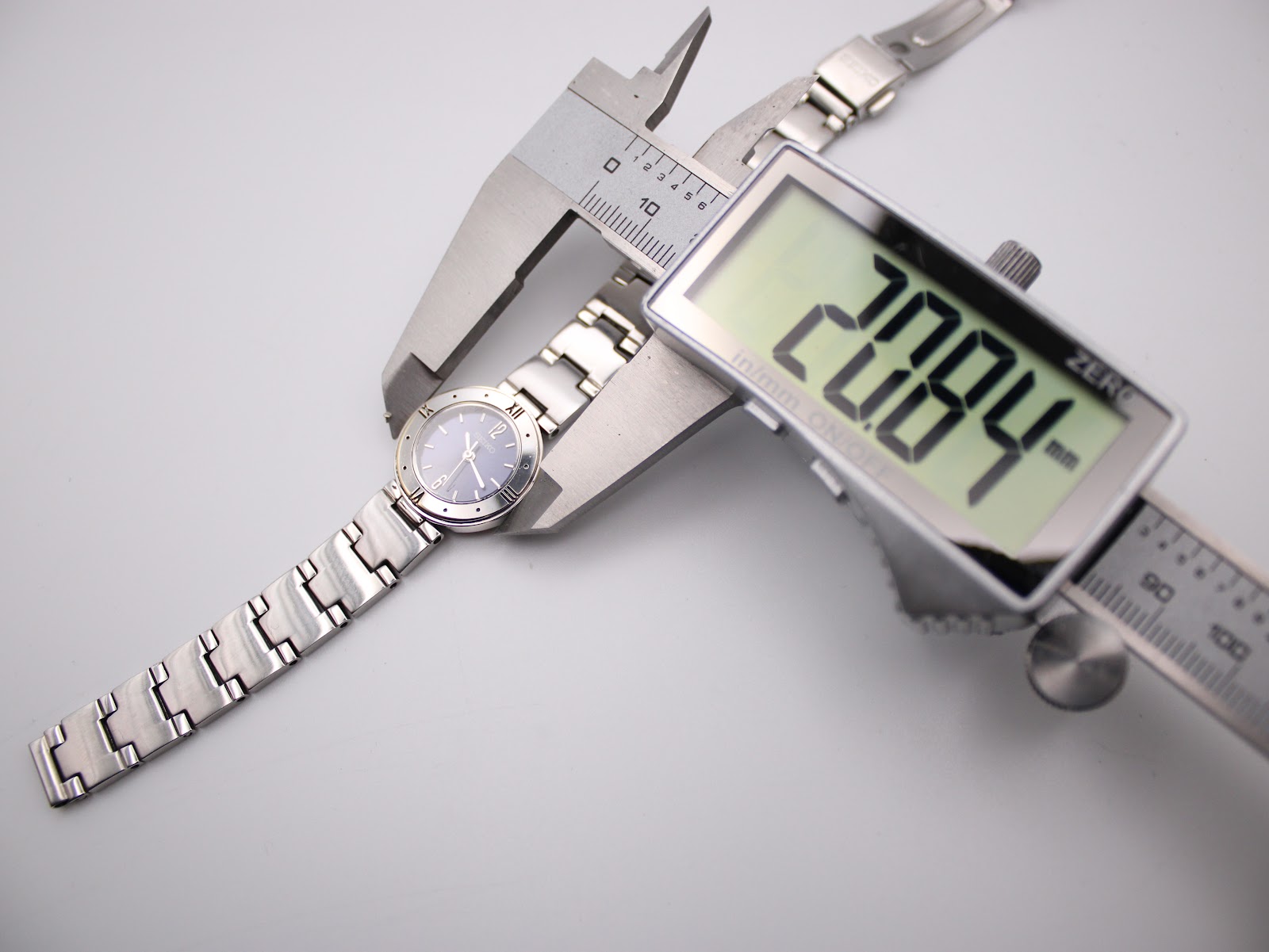 Overhead view of the Seiko watch being measured by a digital caliper, displaying a case size of 20.84mm.