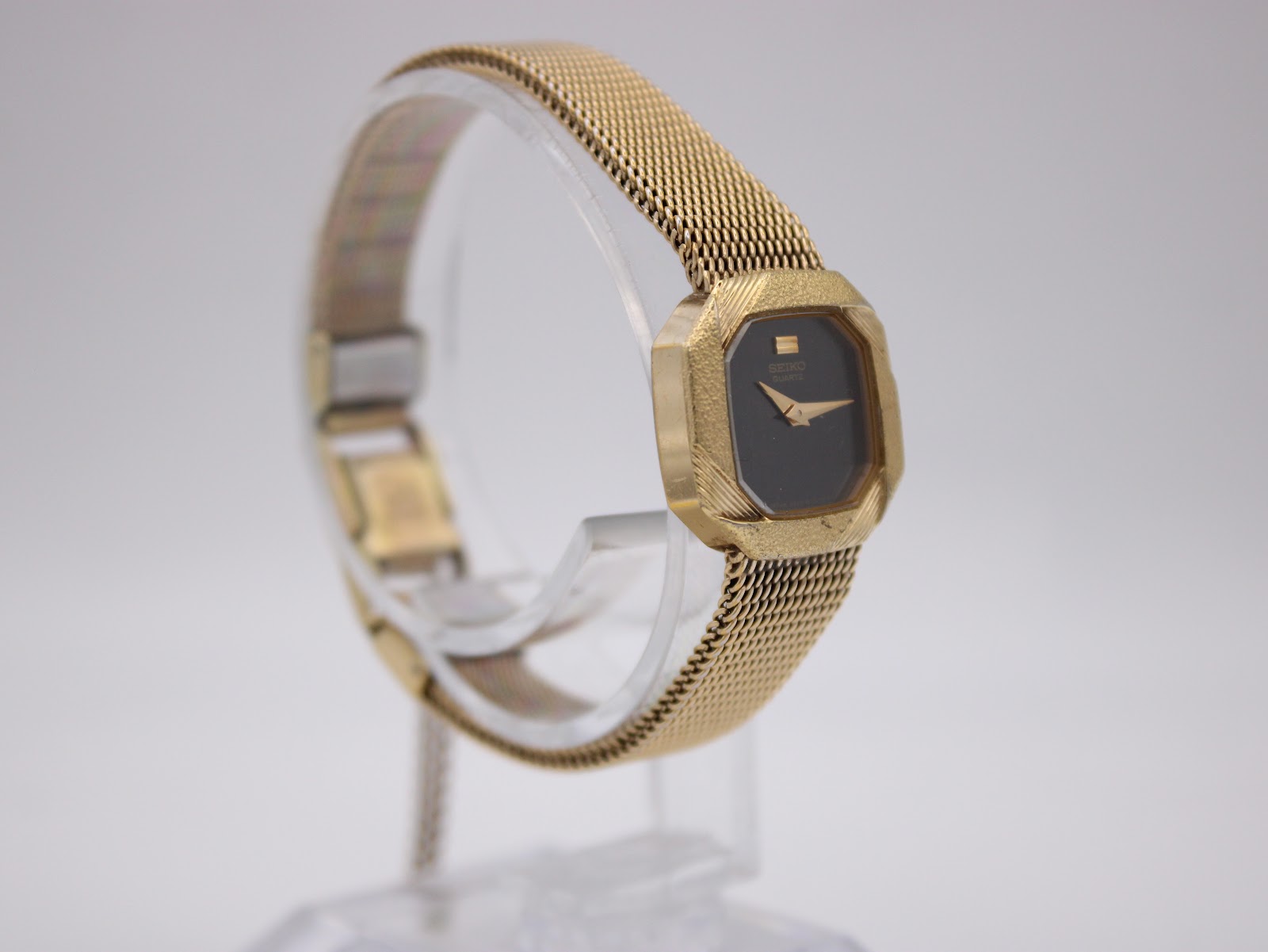 Close-up view of the gold-toned folding clasp and safety chain on the mesh bracelet.