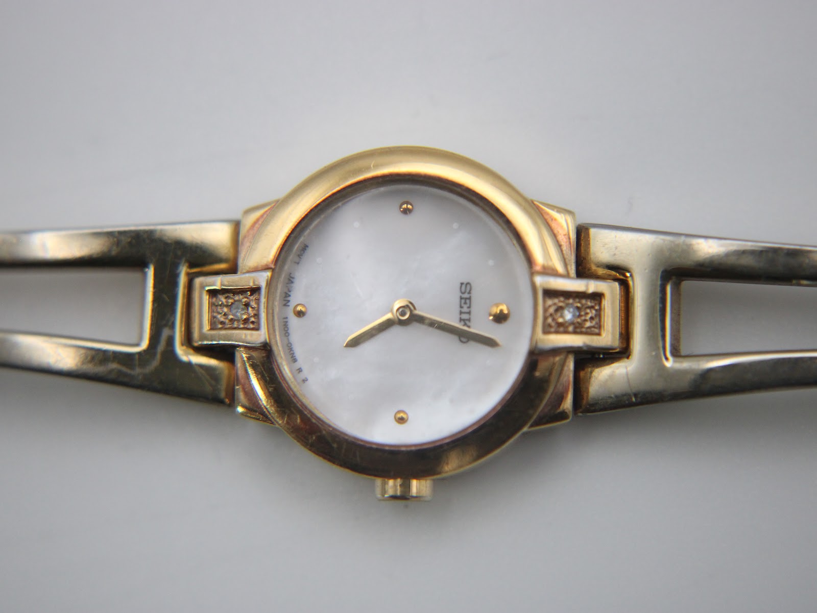 Close-up of the watch dial, clearly showing the mother of pearl finish, gold-tone dot indices, hands, and the small clear stone accents on the lugs.