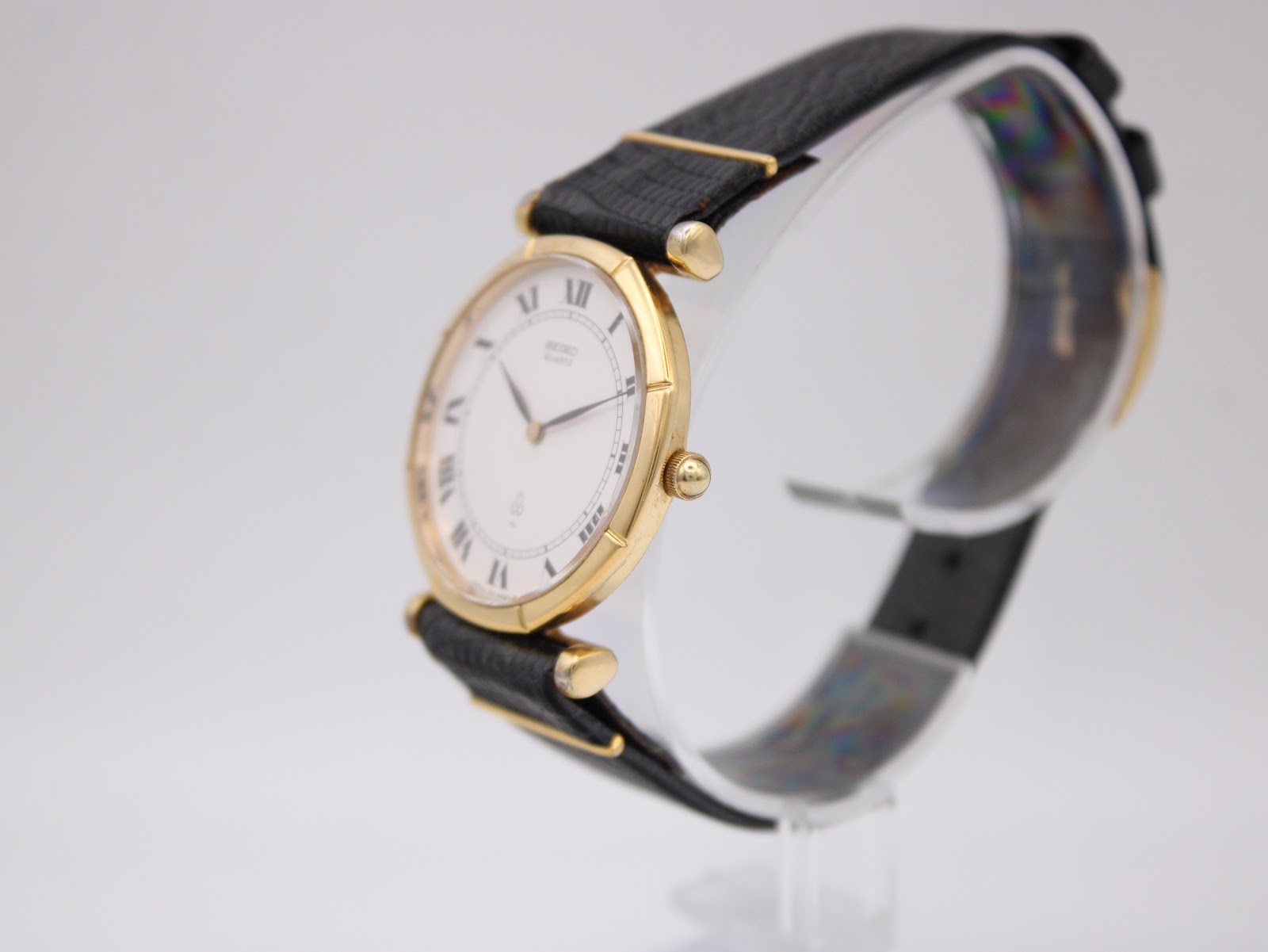 Right side profile view of the Seiko watch, highlighting the slim gold-plated hexagonal case and crown on a clear watch stand.