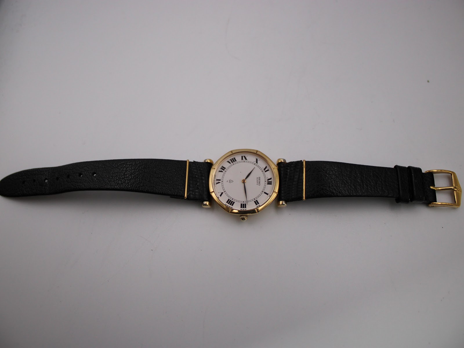 Full overhead view of the Seiko watch with its black lizard-grain leather strap and gold-tone tang buckle laid flat.