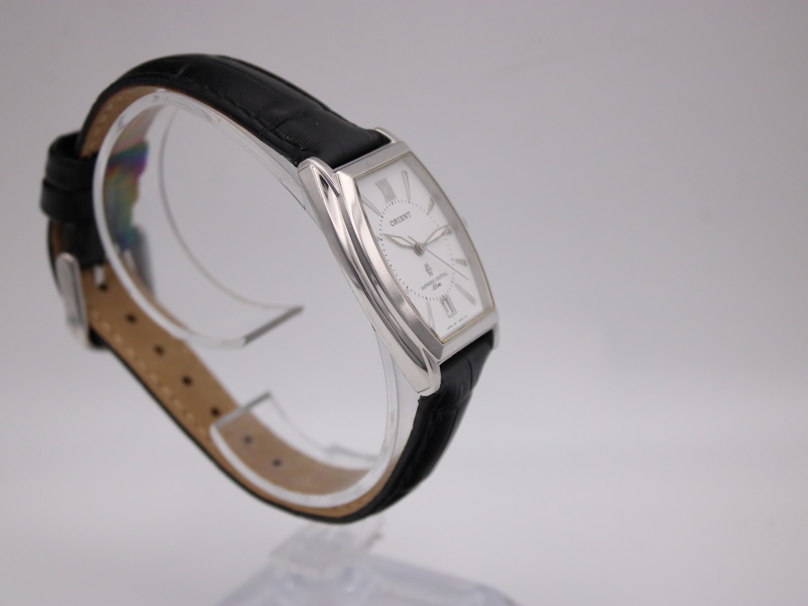 Angled side view of the Orient UNBH-CO watch on a stand, highlighting the case shape and the texture of the black leather strap.