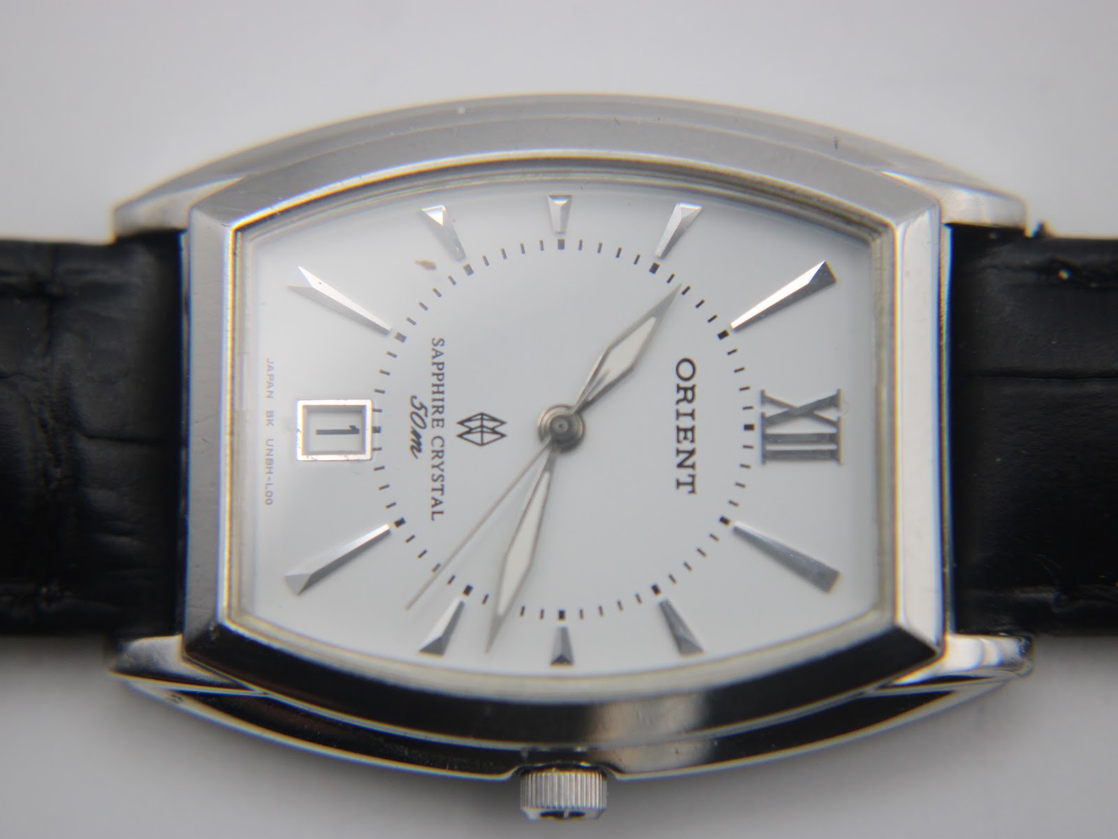 Close-up front view of the white dial of the Orient UNBH-CO watch, showing baton indices, Roman numeral at 12, date window at 6, and "Sapphire Crystal 50m" text.