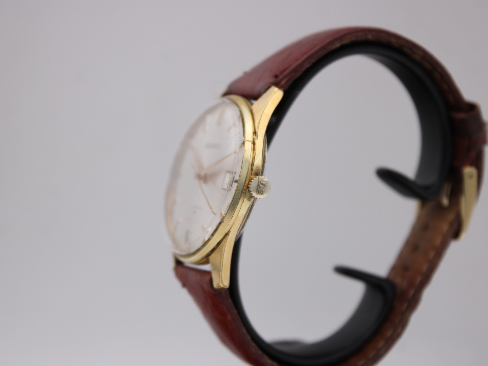 Side profile view of the gold plated Seiko watch on a display stand, showing the crown and domed acrylic crystal.