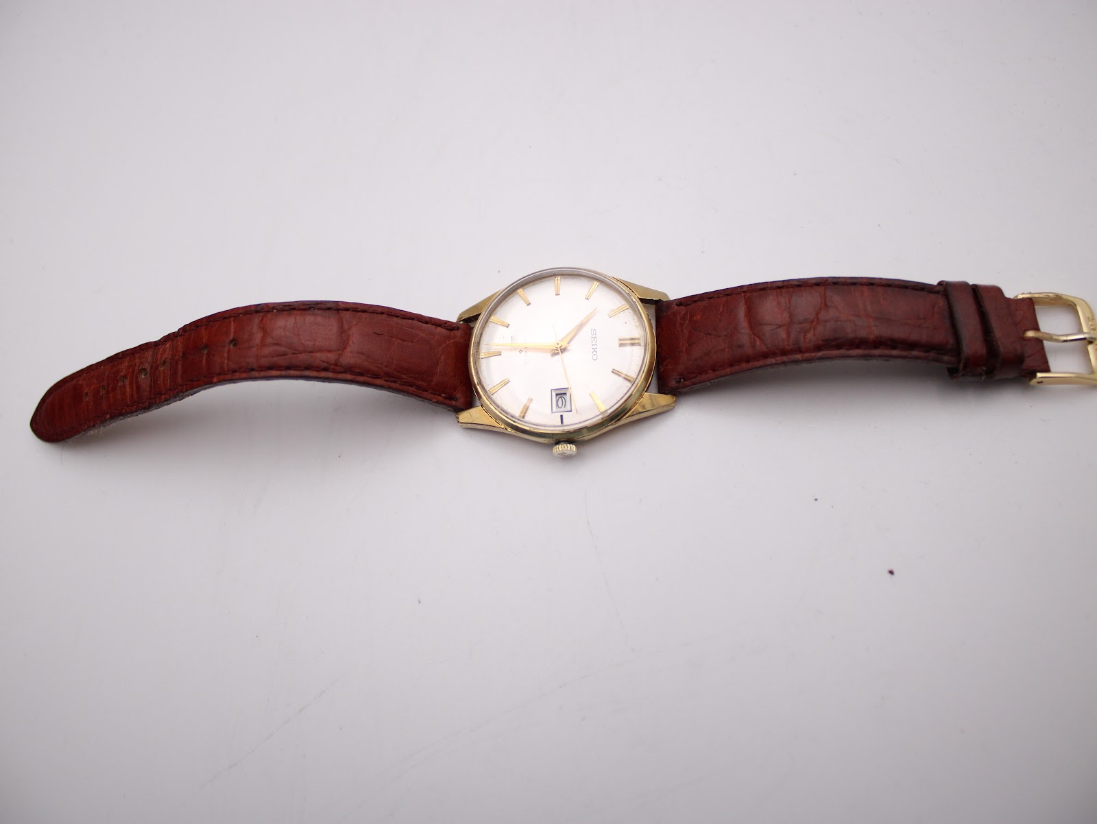 Full front view of the Seiko watch with the brown leather strap laid flat on a white surface.