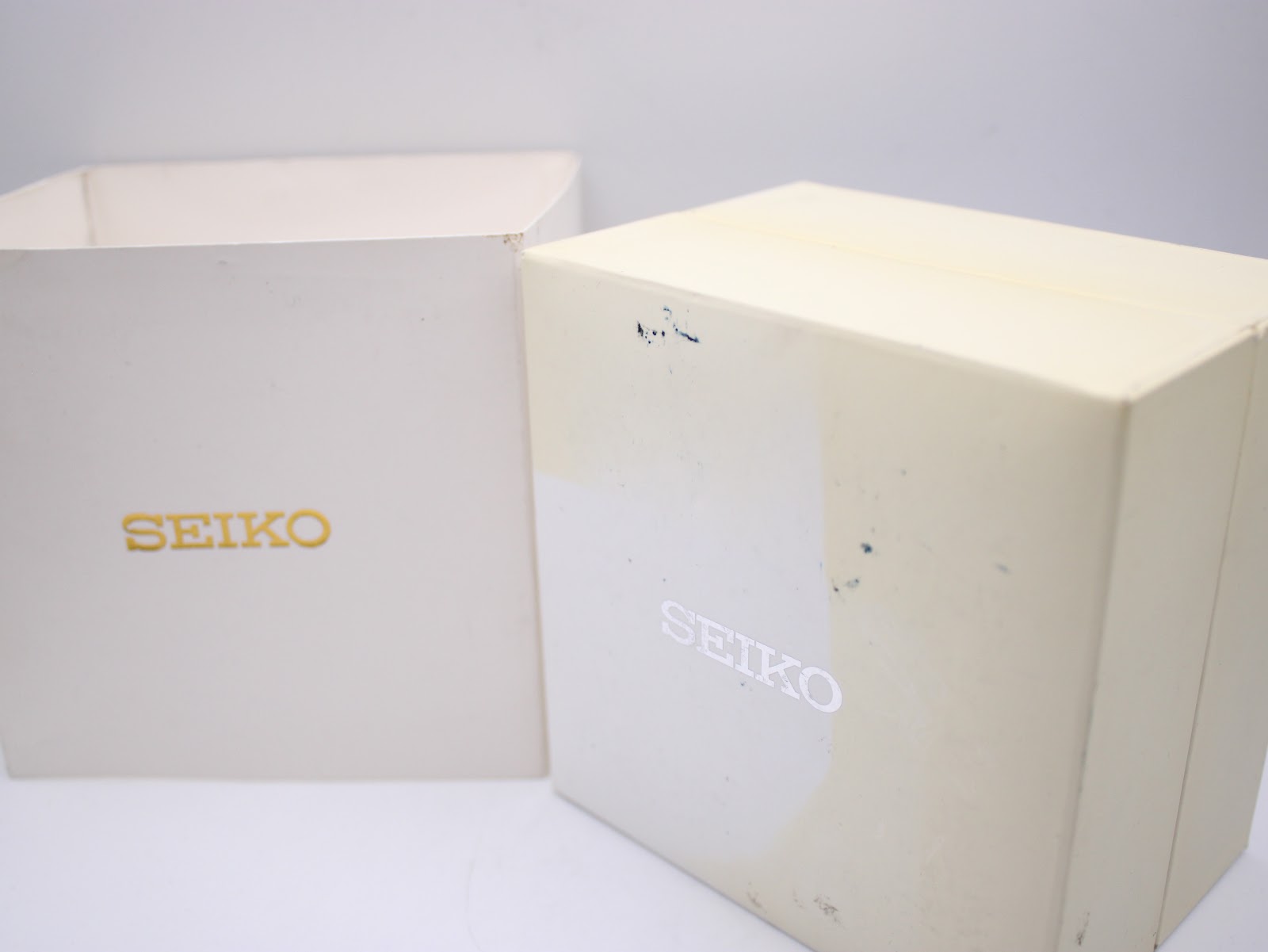 Two parts of the original Seiko watch box, an inner white box with "SEIKO" in gold and an outer white box with "SEIKO" in silver, showing some wear.