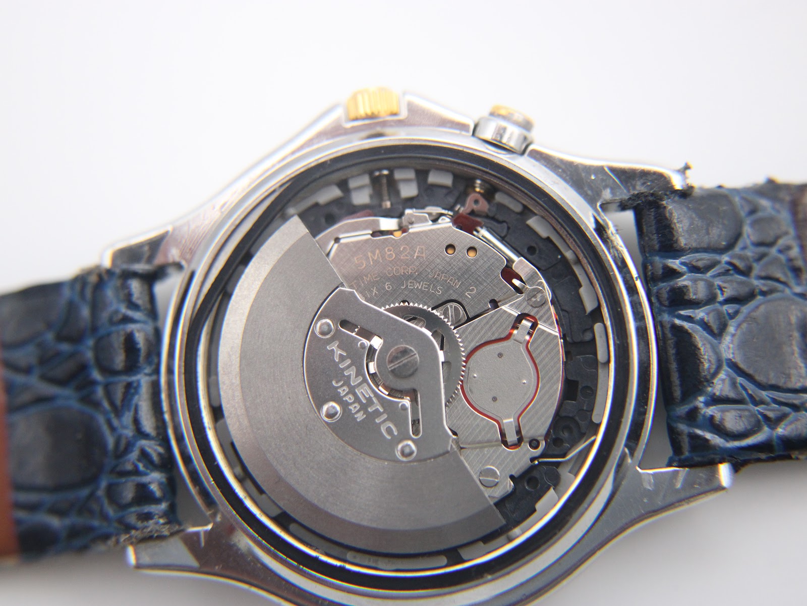 Macro shot of the Seiko 5M82A kinetic movement visible inside the open case back, showing the rotor and jewels.