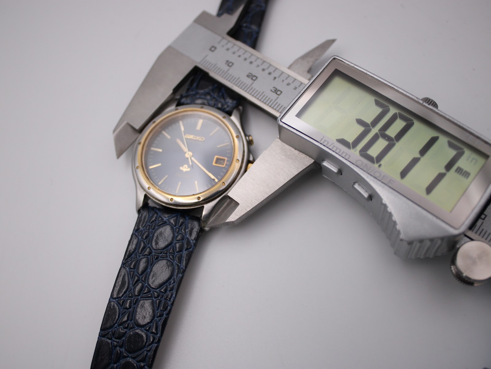 Digital caliper measuring the case diameter of the Seiko Kinetic watch at 38.17mm from a top-down angle, showing the full dial.
