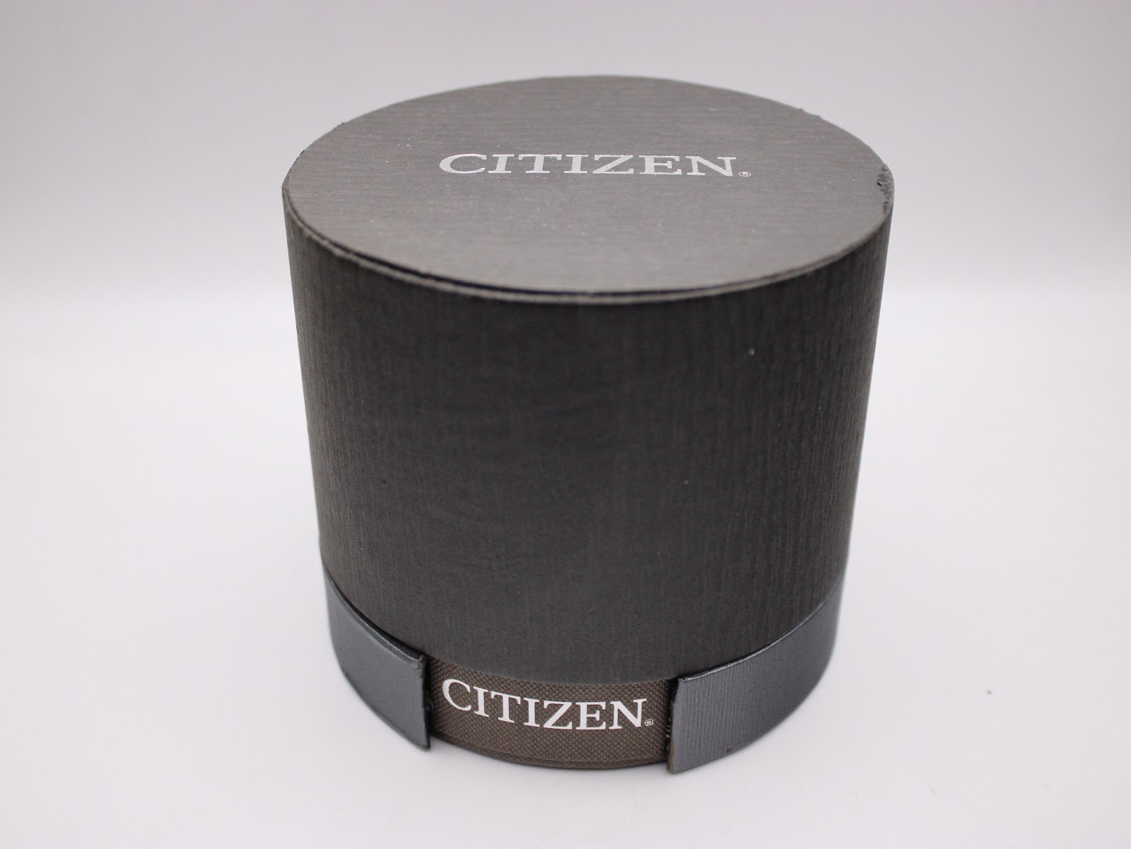 Top view of the closed dark grey circular Citizen original watch box with 'CITIZEN' logo on the side.