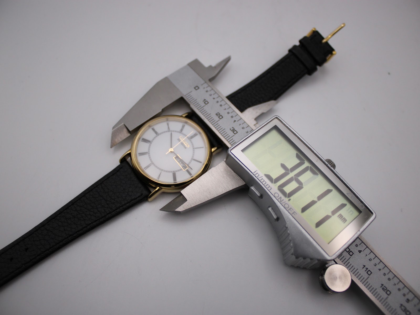 Top-down view of the Citizen Eco-Drive watch being measured by a digital caliper, displaying a case diameter of 36.14mm.