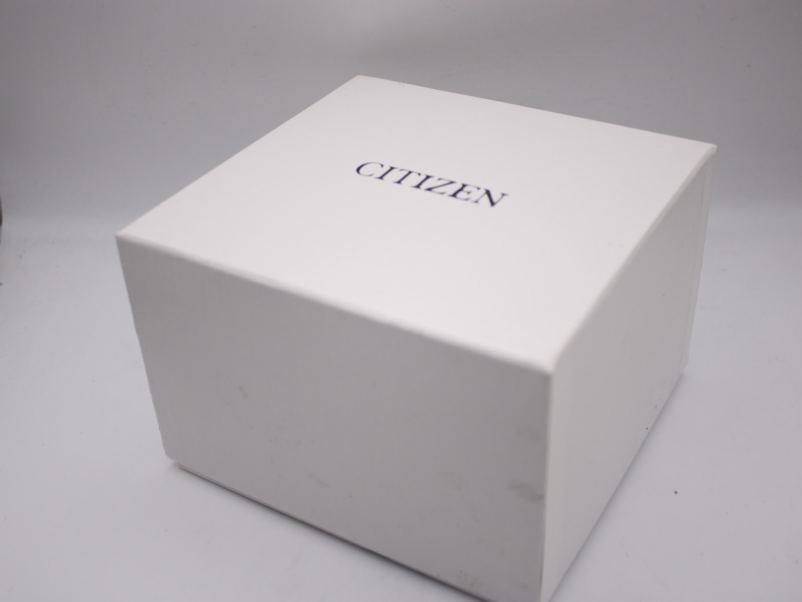 External view of the closed original white Citizen watch box with the brand name printed on top.