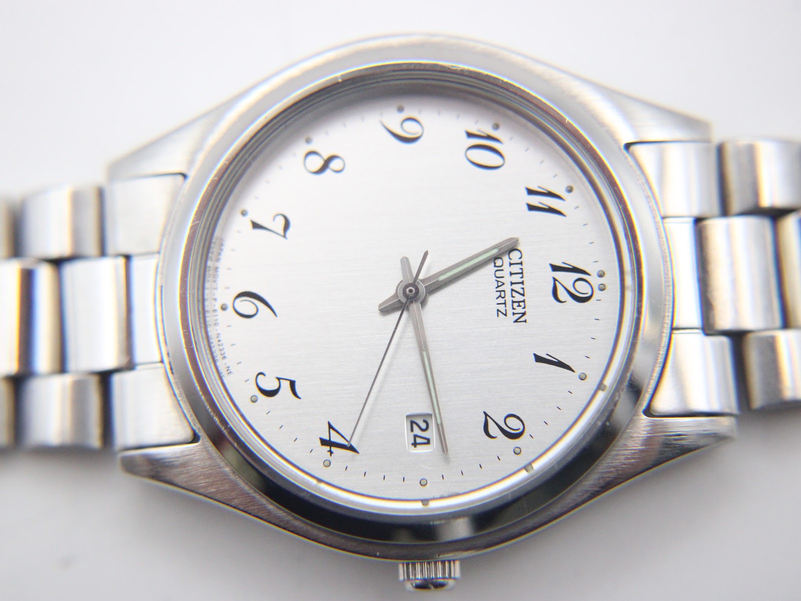 Close-up detailed view of the Citizen watch's silver dial, showing the Arabic numerals, minute track, and date window.