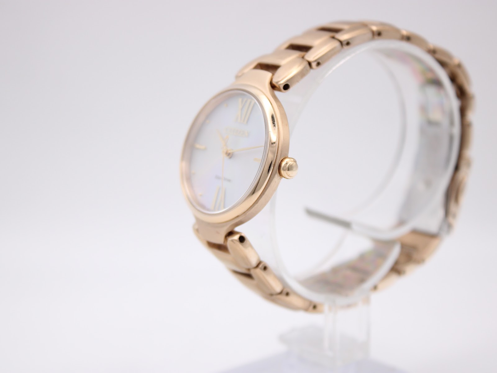 Side view of the rose gold tone Citizen Eco-Drive watch on a clear display stand, showing the case profile and bracelet links.