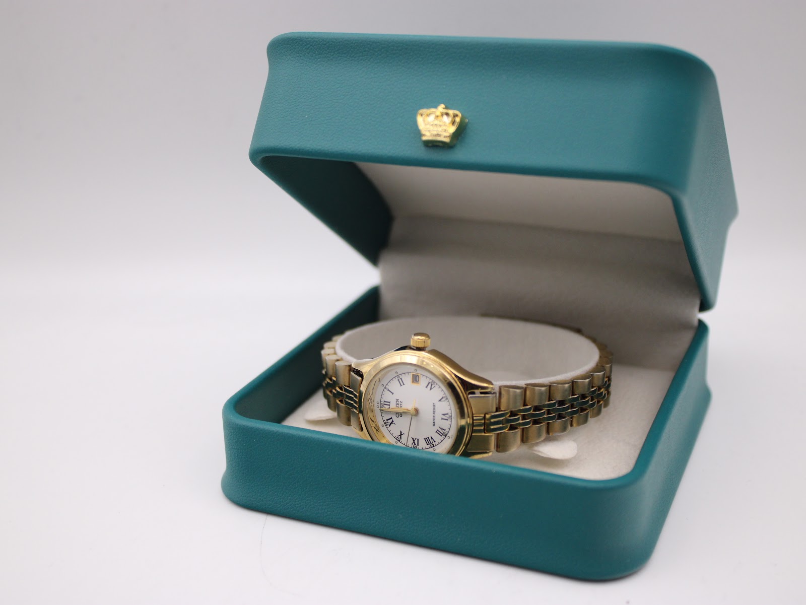 The Citizen watch resting inside its original teal-coloured Citizen watch box with a gold crown emblem.