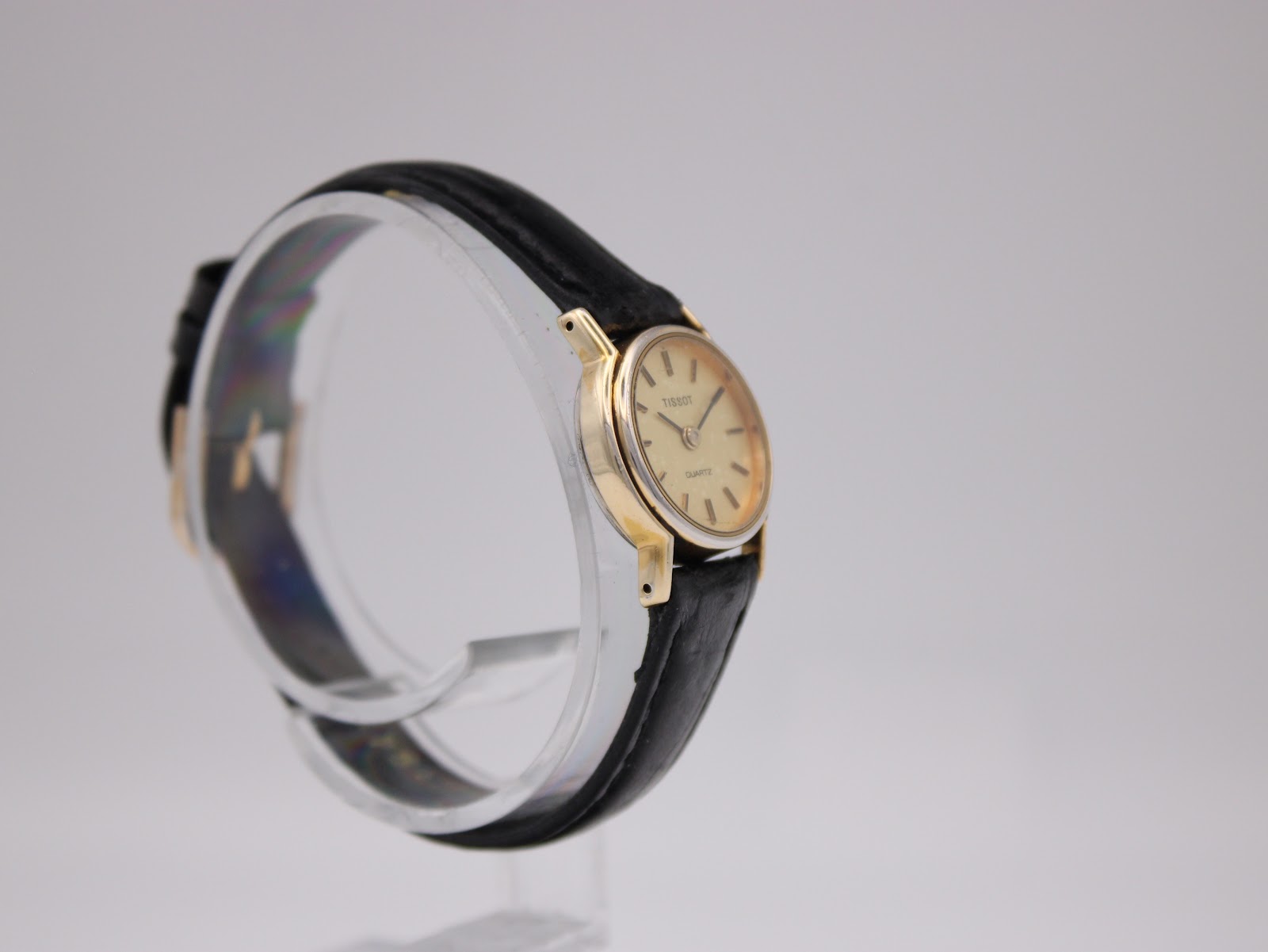 Another side-angle view of the Tissot watch on a stand, showing the curvature of the case and strap.