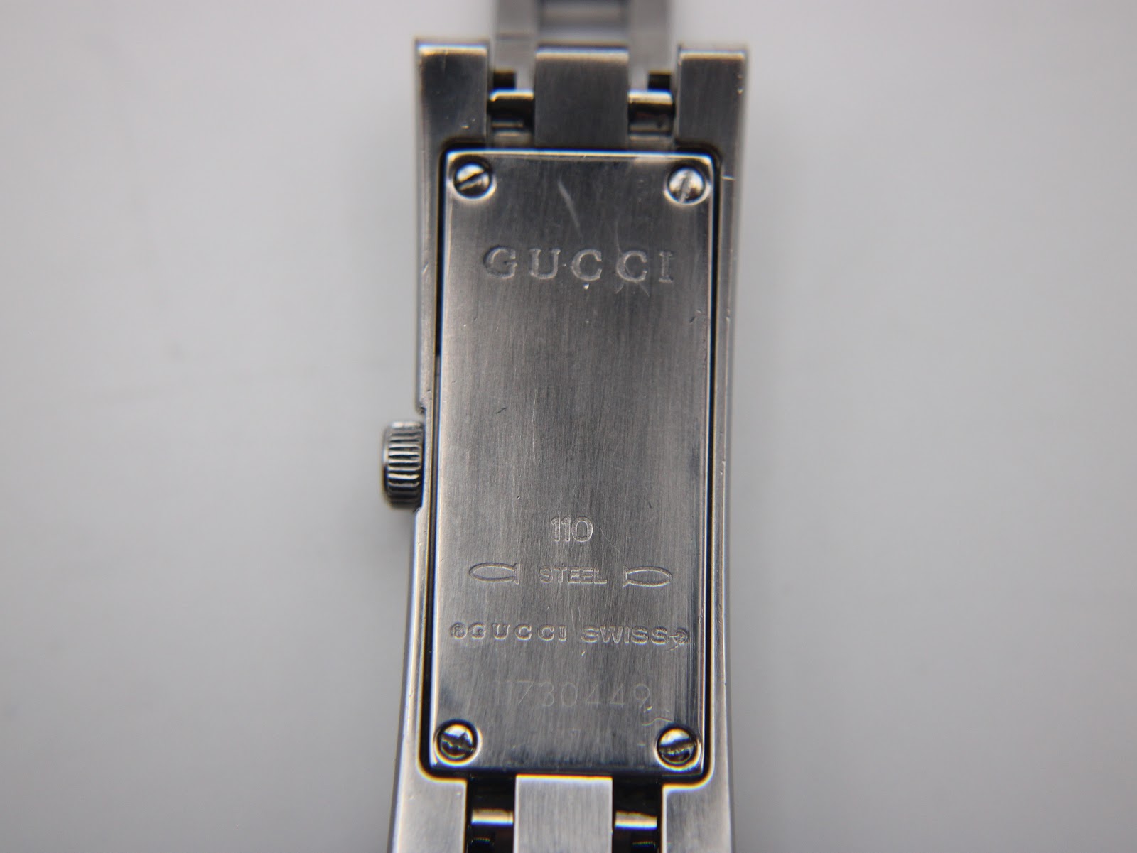 Close-up of the brushed stainless steel case back of the Gucci 110, showing 'GUCCI', '110', 'STEEL', 'SWISS' and serial number.