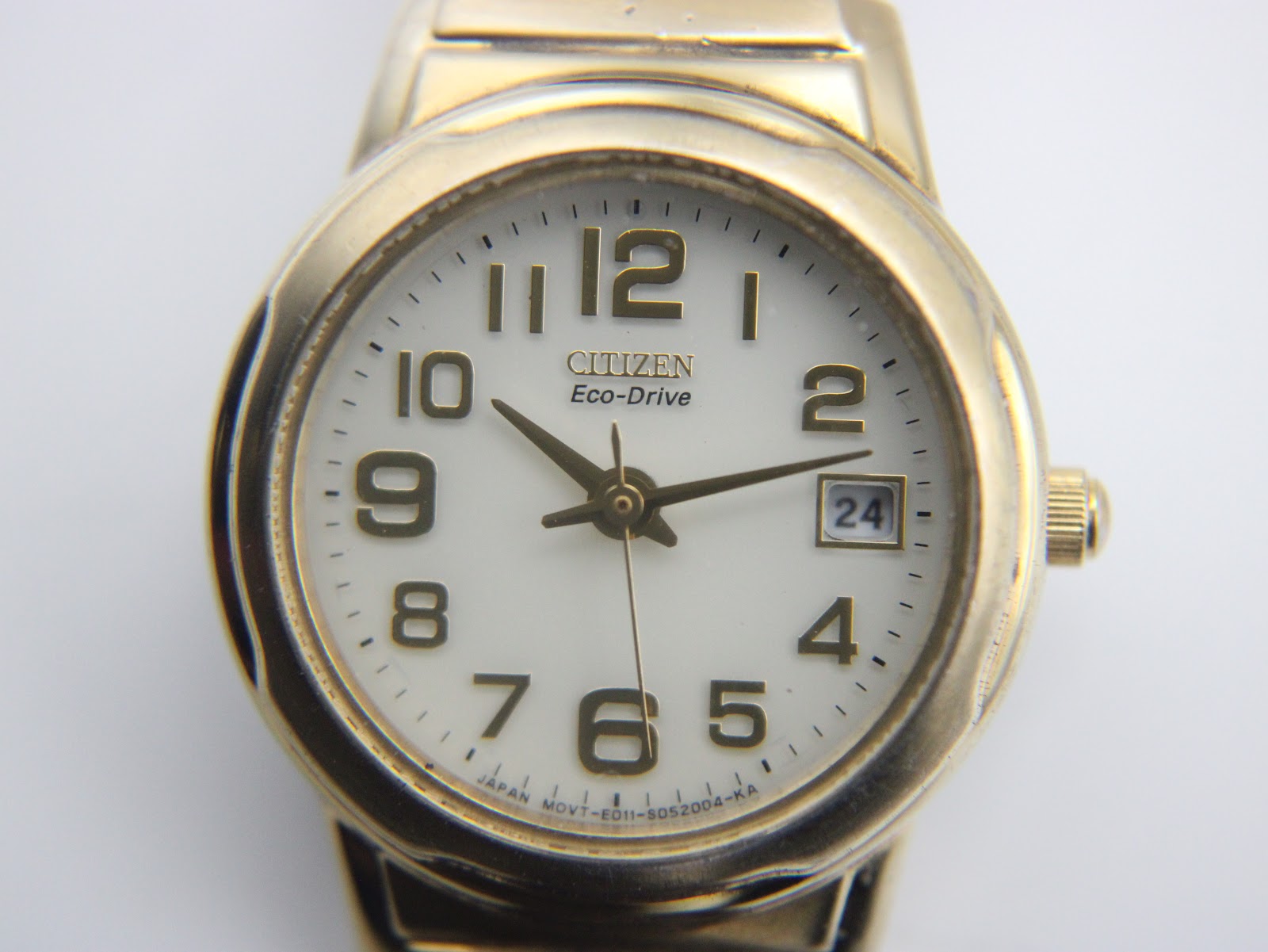 Detailed close-up of the Citizen Eco-Drive white dial, featuring gold-tone arabic numerals, hands, date window, and 'Eco-Drive' text.