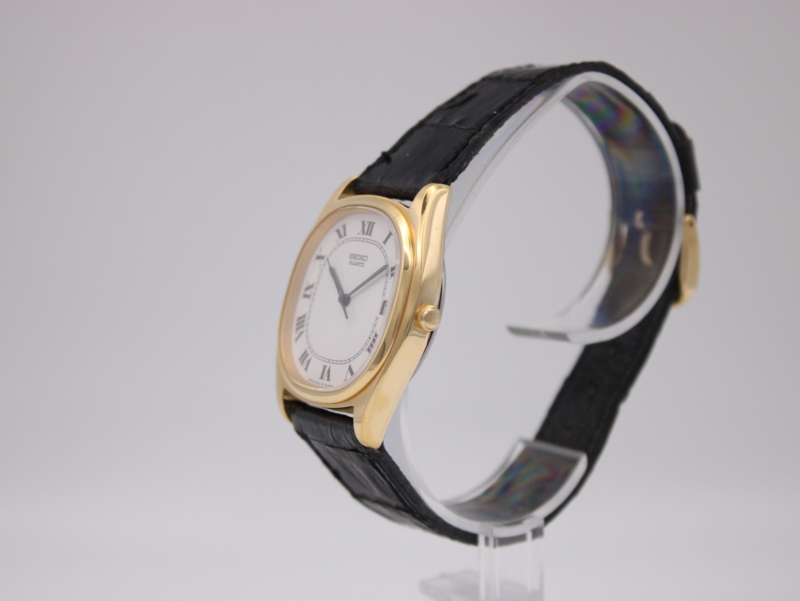 Angled side view of the gold-plated Seiko watch, showing the crown and the profile of the tonneau case and black leather strap.