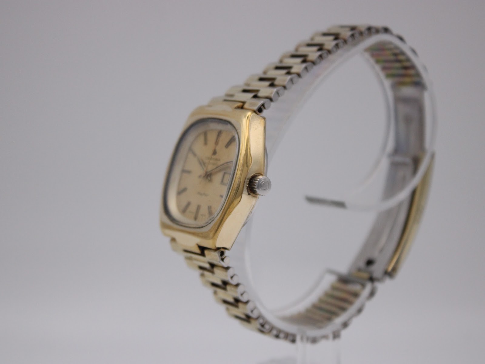 Angled side view of the Certina Mayfair watch, highlighting the case profile, crown, and gold-plated bracelet on a display stand.