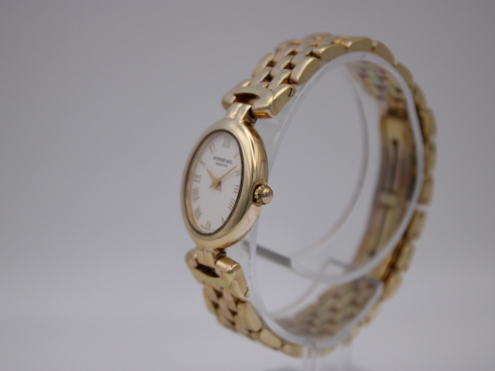 Angled side view of the Raymond Weil 5889 watch, showing the oval gold-tone case, crown, and integrated gold-tone bracelet.