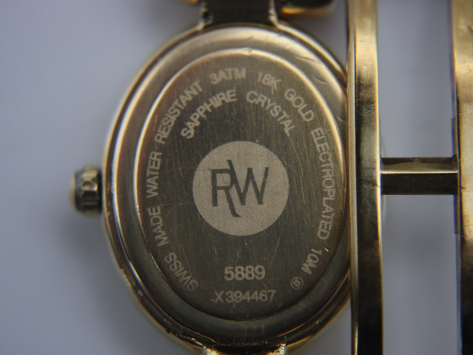 Close-up of the watch case back, showing 'RAYMOND WEIL', model 5889, serial, 18k gold electroplated, 3ATM water resistant, and sapphire crystal markings.