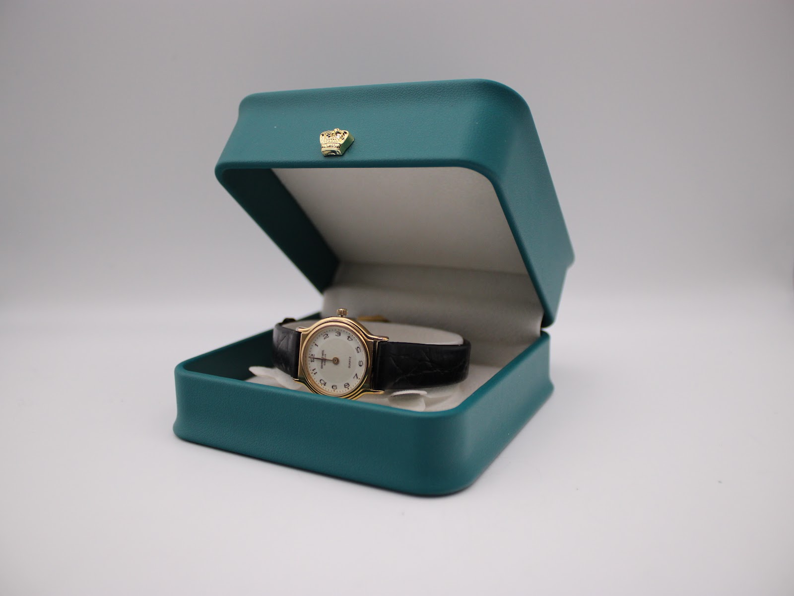 Raymond Weil watch displayed open in a teal presentation box.