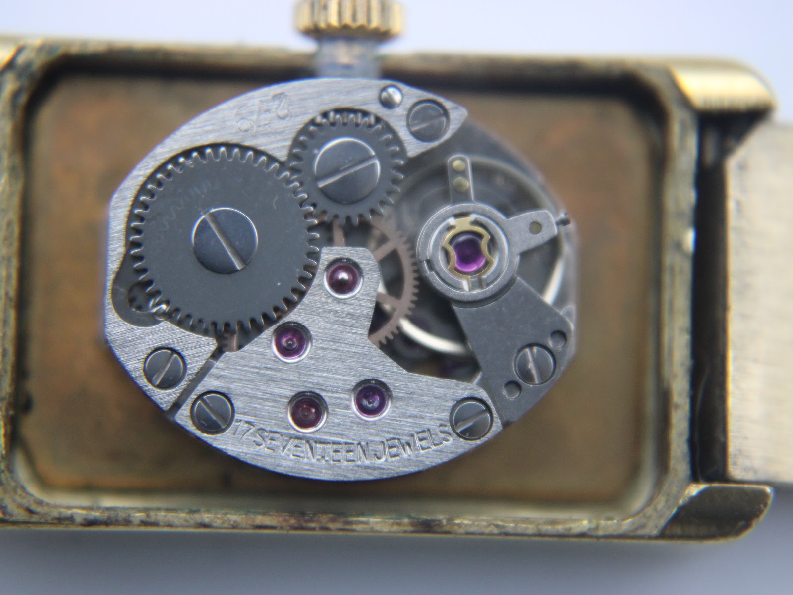 Macro shot of the manual wind movement, showing gears, jewels, and '17 SEVENTEEN JEWELS' engraving.