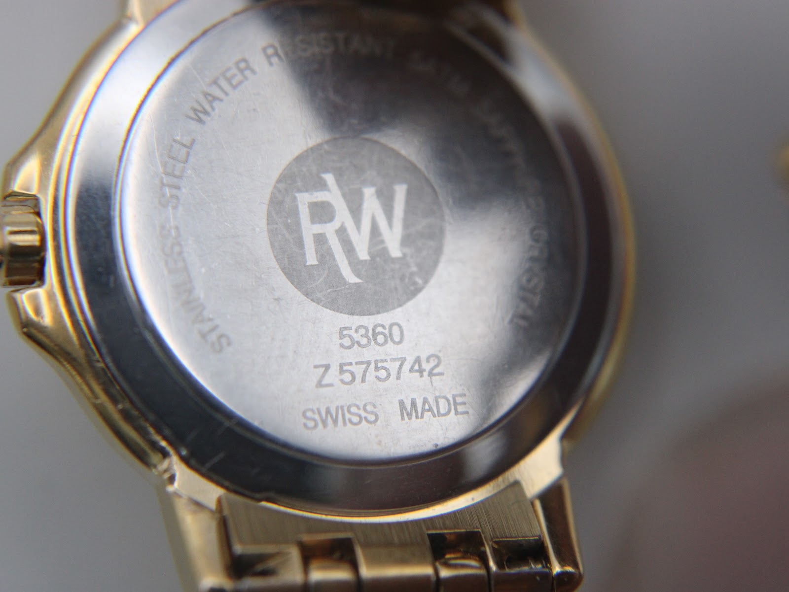 Close-up of the watch case back showing 'RW' logo, model 5360, serial Z 575742, 'stainless steel water resistant 5 ATM sapphire crystal swiss made'.