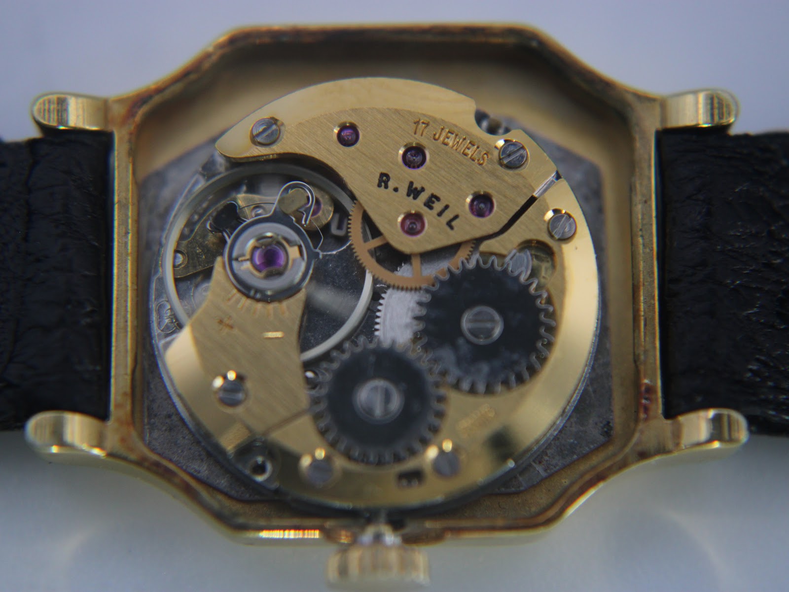 Macro shot of the watch's manual wind movement, displaying the gold-toned plates and 'R. WEIL 17 JEWELS' inscription.